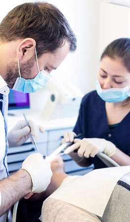 Zahnarzt und Assistentin behandeln Patienten im modernen Behandlungszimmer der Zahnarztpraxis.