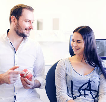 Zahnarzt erklärt Patientin mit Zahnmodell die Zahngesundheit im Behandlungszimmer.